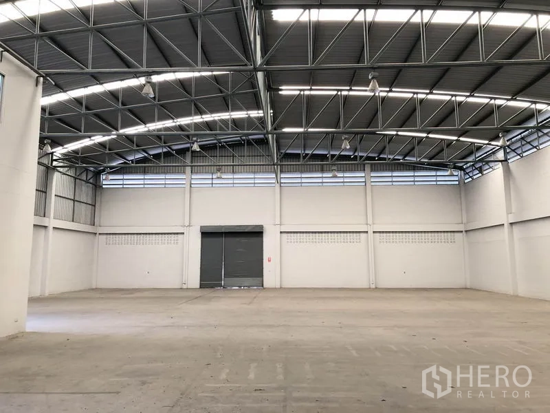 Factory for rent in Pathum Thani - Spacious warehouse interior with high arched steel roof and roller door.