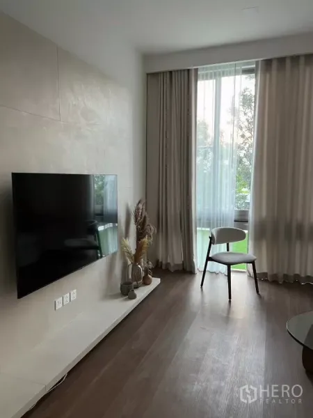 Detached House for rent in Saphan Sung, Bangkok - TV feature wall with floating shelf, tall curtained windows and a single accent chair.