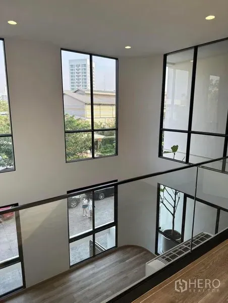 Townhouse for rent in Yan Nawa, Bangkok - Upper landing with glass railing overlooking a double-height atrium and tall windows.