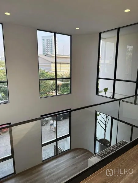 Townhouse for rent in Yan Nawa, Bangkok - Upper landing with glass railing overlooking a double-height atrium and tall windows.