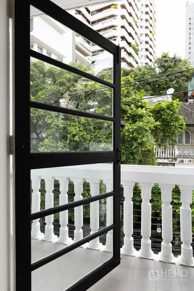 ทาวน์เฮาส์ ให้เช่าในKhlong Toei, Bangkok - ระเบียงขนาดกะทัดรัด ราวลูกกรงสีขาวและประตูกรอบอลูมิเนียมสีดำ มองเห็นต้นไม้และอาคารใกล้เคียง