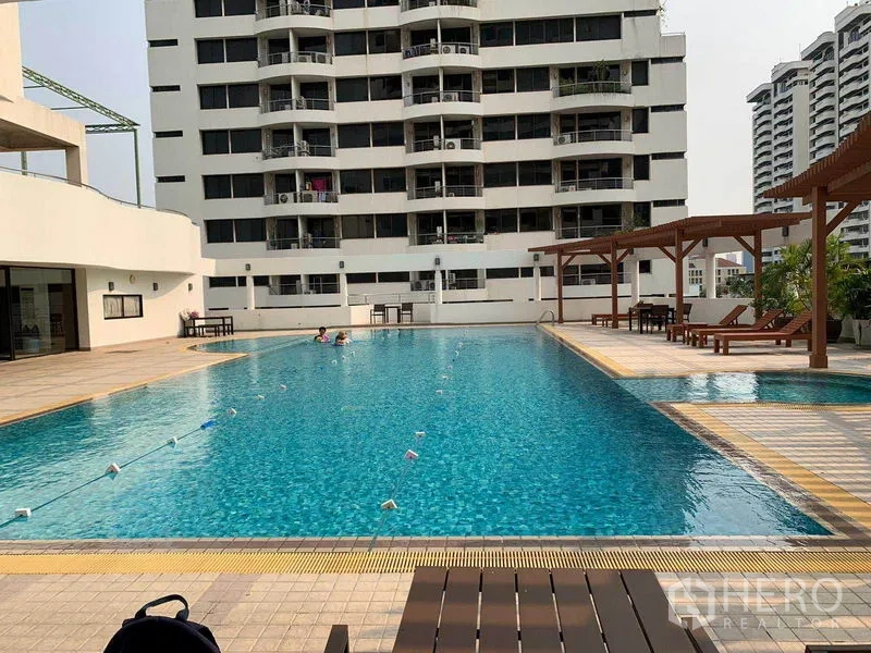 Condominium for rent or sale in Watthana, Bangkok - Outdoor swimming pool with sundeck loungers and city-view condominium facade.