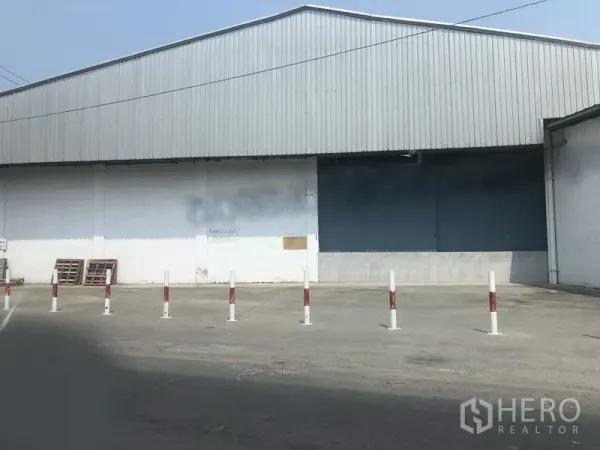 货栈 出租在Nonthaburi - 仓库外立面，带装卸卷帘门、防撞桩与宽阔硬化场地