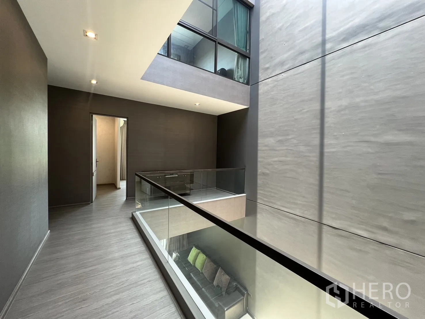 Townhouse for rent in Lat Phrao, Bangkok - Upper corridor wrapping central void with glass railing and grey flooring.