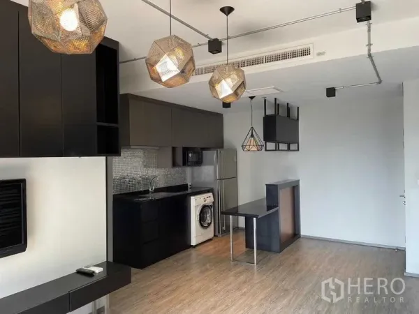 Condominium for sale in Phaya Thai, Bangkok - Modern open-plan kitchen with black cabinetry, pendant lights, and washer in Phaya Thai condo.