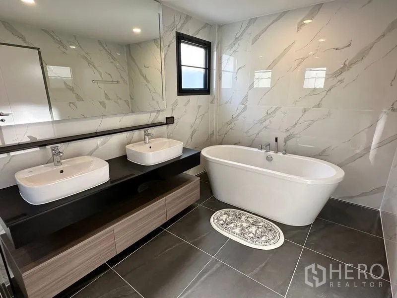Detached House for rent or sale in Bang Phli, Samut Prakan - Modern bathroom with freestanding tub, double vanity and marble walls.