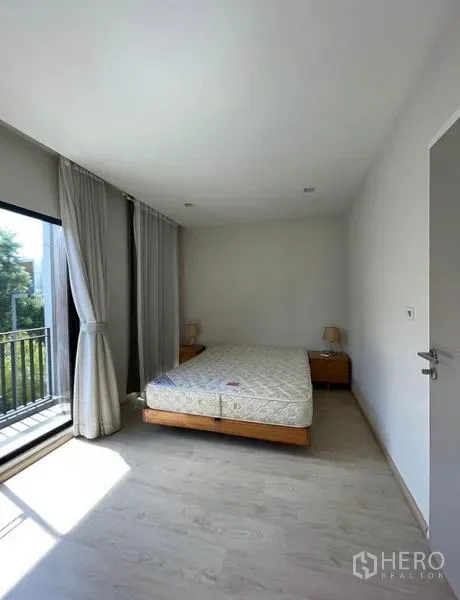 Townhouse for rent in Yan Nawa, Bangkok - Bright bedroom with queen bed, light wood floor, and floor-to-ceiling curtains opening to a small balcony.