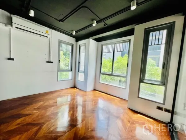 办公空间 出租在Khlong Toei, Bangkok - 转角办公室，鱼骨拼木地板、黑色天花，多扇窗户面向绿树。