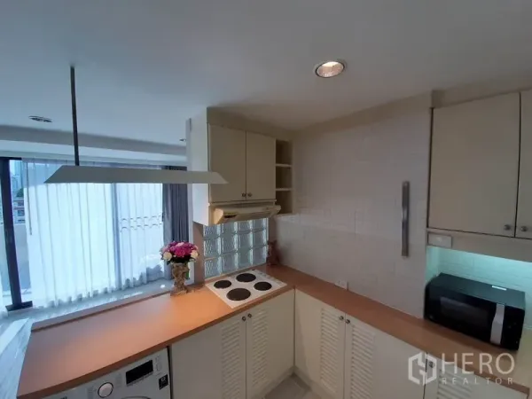 公寓 出租或出售在Watthana, Bangkok - 明亮的U形厨房，电炉、抽油烟机、白色橱柜与窗边采光。