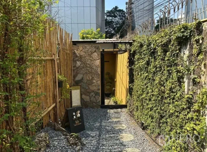 Retail Space for rent in Khlong Toei, Bangkok - Narrow gravel walkway between a bamboo fence and an ivy-covered wall leading to an entrance.