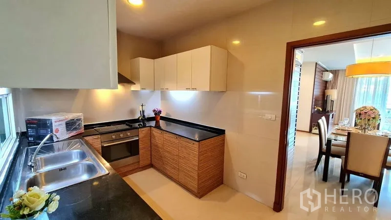Apartment for rent in Khlong Toei, Bangkok - Kitchen view toward the dining area with ample cabinets and under-cabinet lighting.
