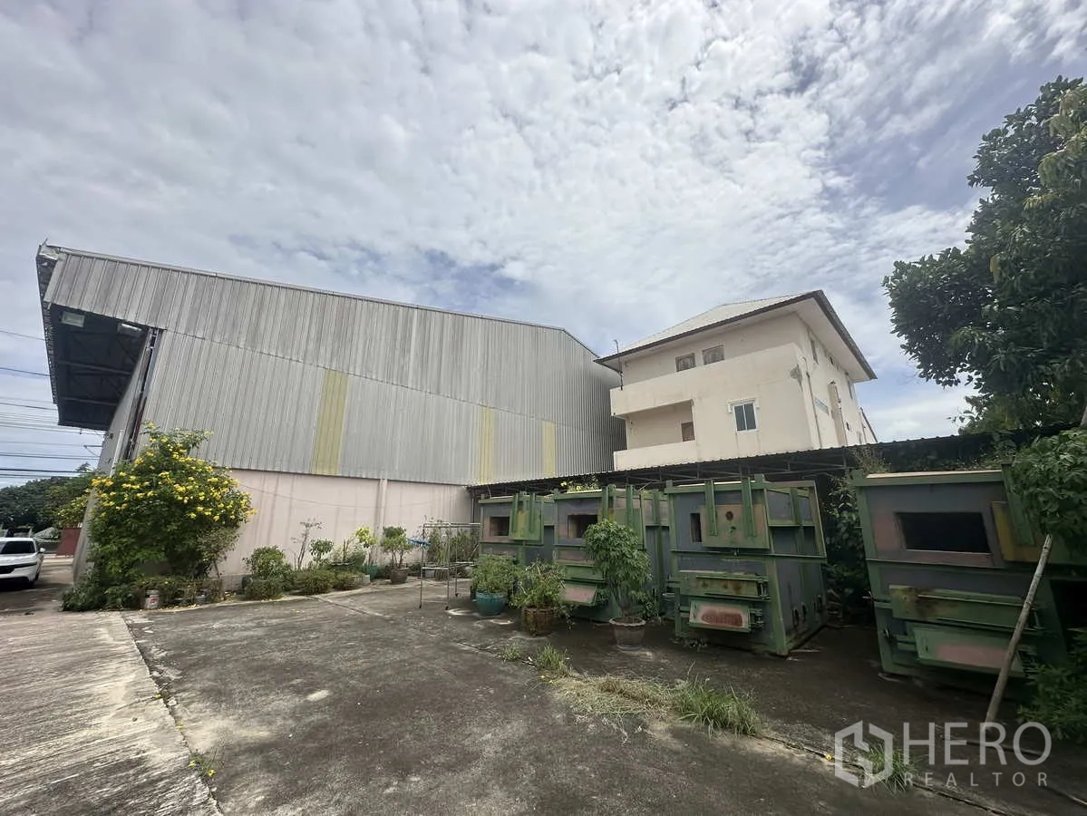 Factory for rent in Pathum Thani - Rear yard beside the metal-clad warehouse with greenery, storage units and parking space.