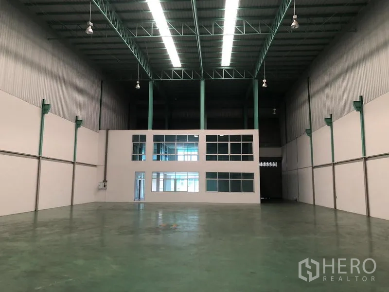 Factory for rent in Samut Prakan - Warehouse interior facing a two‑storey office block with polished floor.