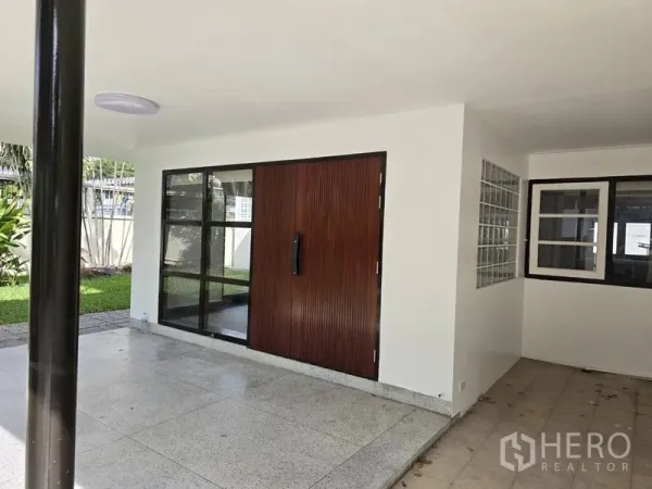 独立式住宅 出租在Watthana, Bangkok - 有顶露台与车棚，木质入户门和黑框窗户。
