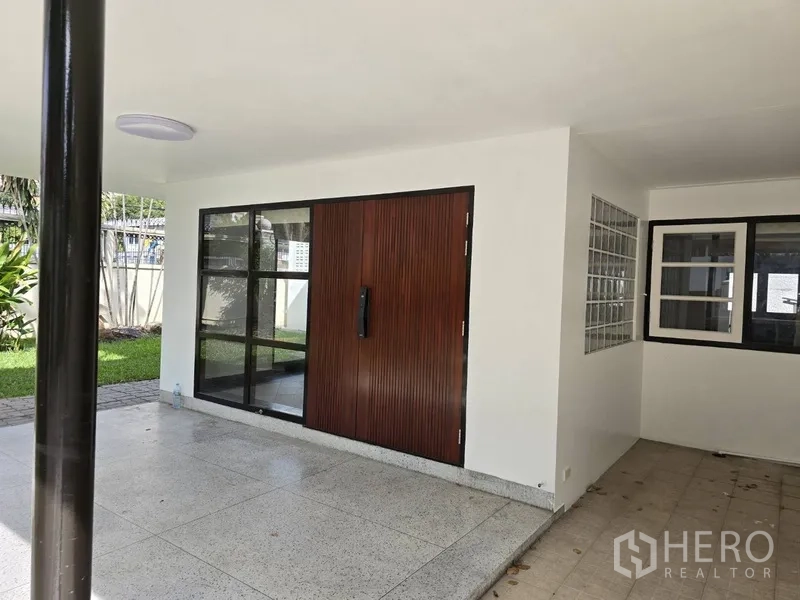独立式住宅 出租在Watthana, Bangkok - 有顶露台与车棚，木质入户门和黑框窗户。