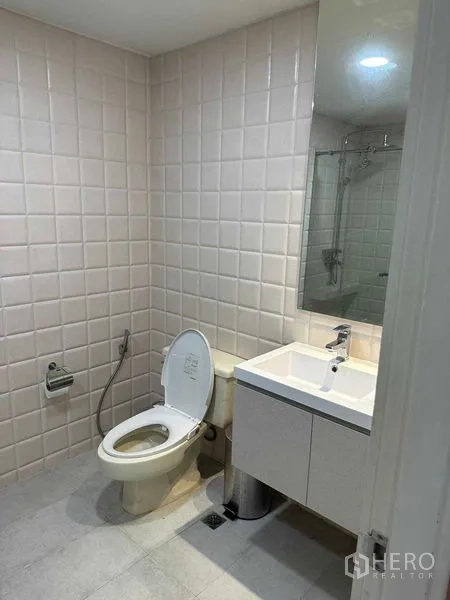 公寓 出租或出售在Bangkok - 卫生间配白色台盆柜、坐便器与瓷砖墙。