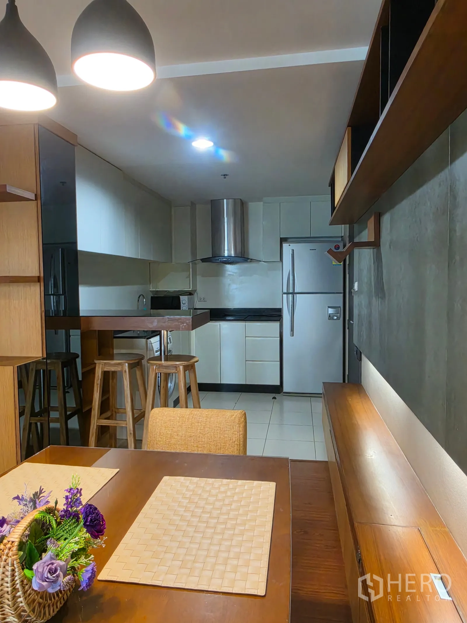 Condominium for rent in Huai Khwang, Bangkok - Dining area with pendant lights, wooden table, and breakfast bar facing the kitchen.
