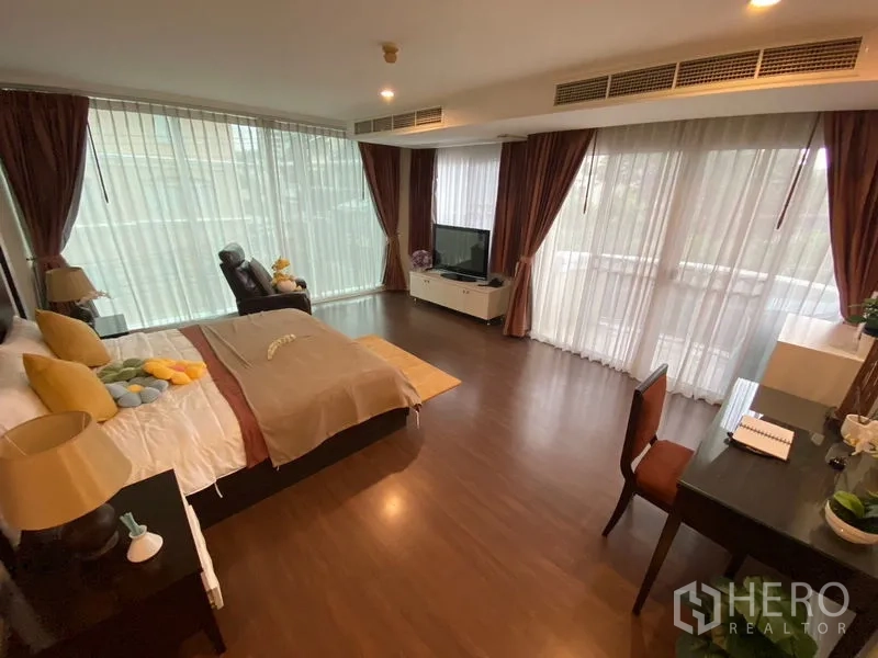 Apartment for rent in Watthana, Bangkok - Large master bedroom with a king bed, lounge chair and full-height curtains.