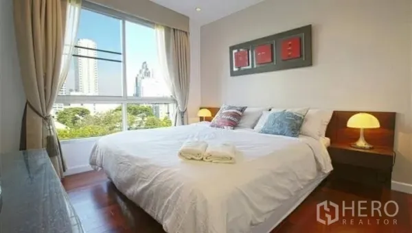 Condominium for rent or sale in Watthana, Bangkok - Cozy bedroom with large window, bedside lamps and a cityscape outlook.