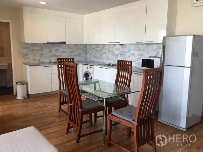 Condominium for rent in Watthana, Bangkok - Dining space with glass table and full kitchen with fridge in the condo.