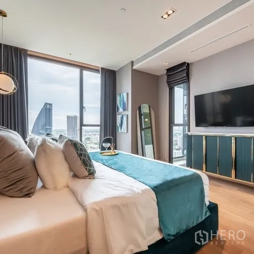 Condominium for rent in Khlong Toei, Bangkok - Master bedroom with teal upholstered headboard, wall-mounted TV and skyline views through full-height glazing.