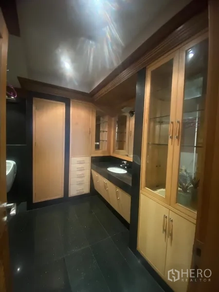 Condominium for rent in Pathum Wan, Bangkok - Bathroom or dressing area with extensive built-in cabinets, vanity and dark tiled floor.