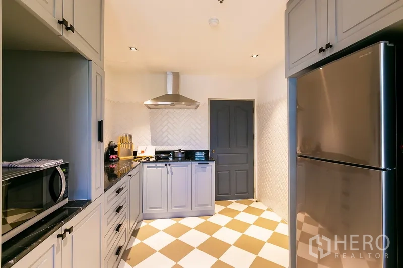 Apartment for rent in Khlong Toei, Bangkok - Full kitchen with grey cabinetry, checkered floor and stainless-steel fridge.
