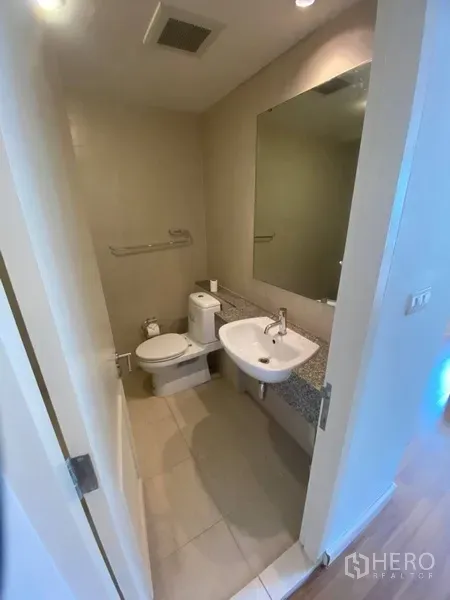 Condominium for rent in Watthana, Bangkok - Compact bathroom with vanity, large mirror, and toilet in neutral tones.