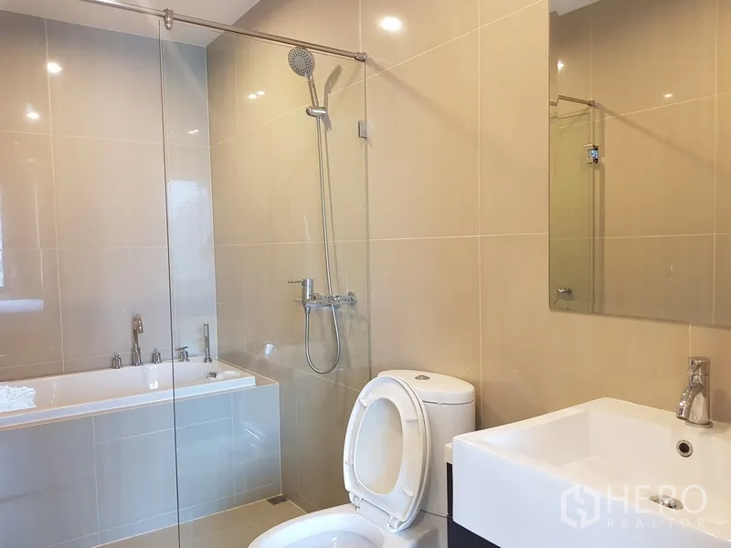 公寓 出租在Ratchathewi, Bangkok - 现代浴室，玻璃淋浴间、浴缸、方形台盆与米色瓷砖。
