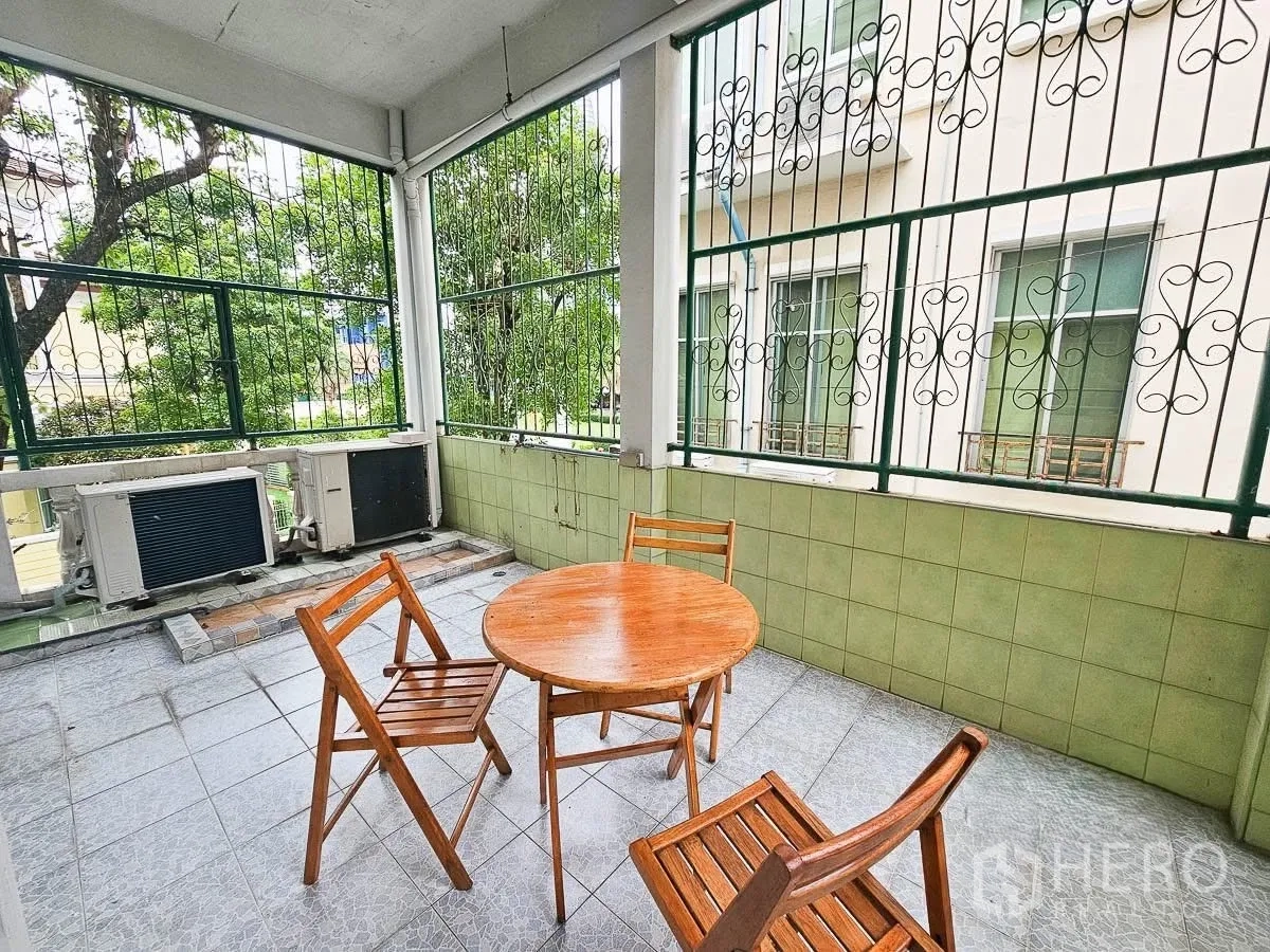 ทาวน์เฮาส์ for rent in Yan Nawa, Bangkok - ระเบียงกึ่งเอาท์ดอร์พร้อมโต๊ะกลมไม้และเก้าอี้สามตัว มองเห็นต้นไม้และคอยล์แอร์