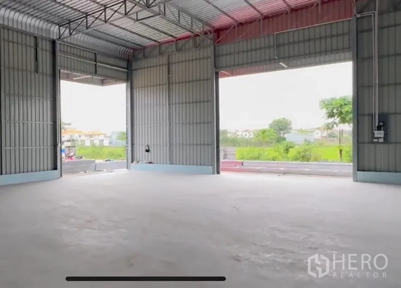 Warehouse for rent in Lam Luk Ka, Pathum Thani - Spacious warehouse interior with high steel roof, wide openings and smooth concrete floor facing greenery.