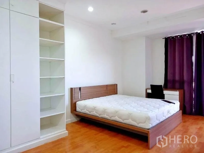 Condominium for rent in Khlong Toei, Bangkok - Bedroom with platform bed, built-in shelving, wardrobe and desk beside curtained window.
