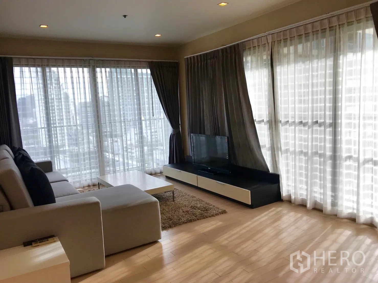 คอนโด ให้เช่าในWatthana, Bangkok - ห้องนั่งเล่นมุมอาคาร พร้อมกระจกเต็มบาน วิวเมือง ตู้วางทีวี พรม และโซฟาตัวแอล