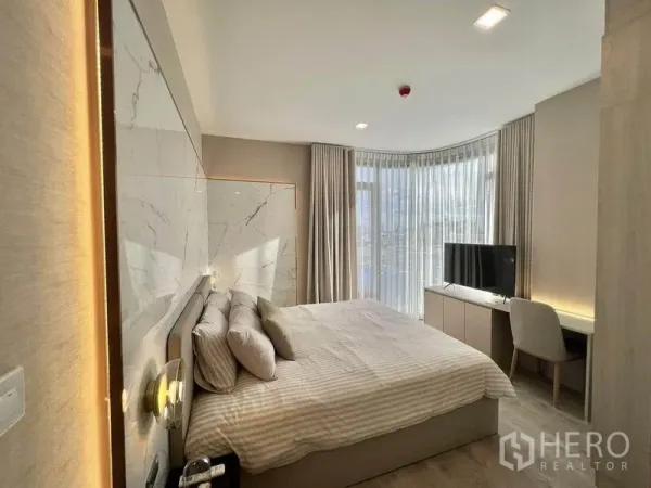 Condominium for rent in Watthana, Bangkok - Bright bedroom with marble headboard, curved full‑height curtains, work desk and TV.