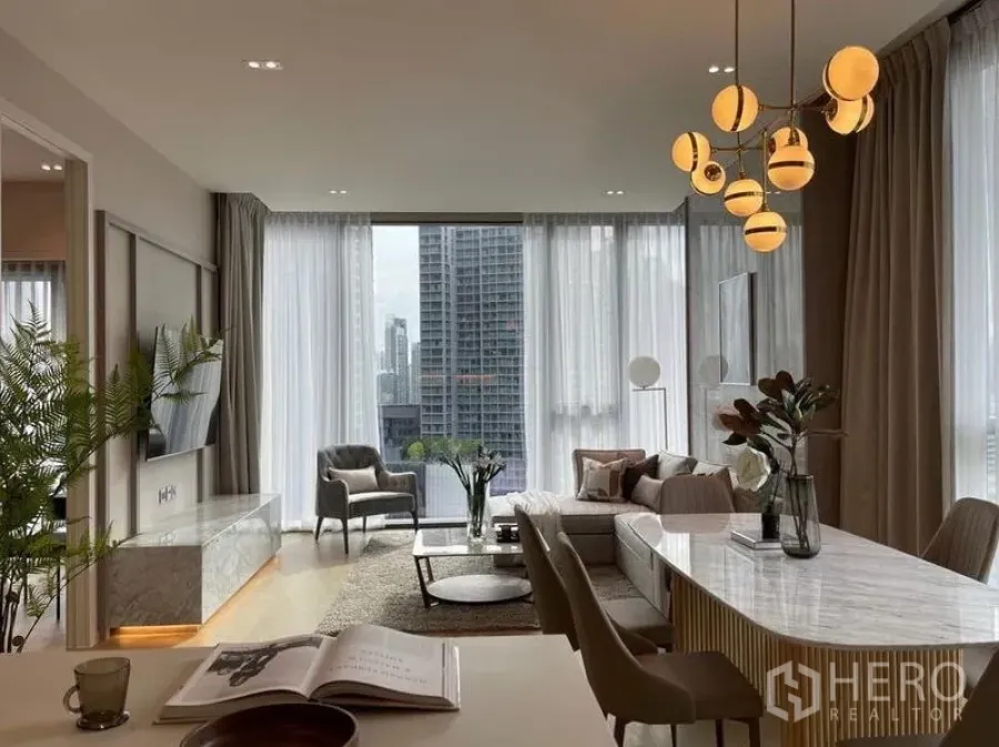 Condominium for rent in Watthana, Bangkok - Open-plan living and dining area with a designer chandelier and tall windows overlooking the city.