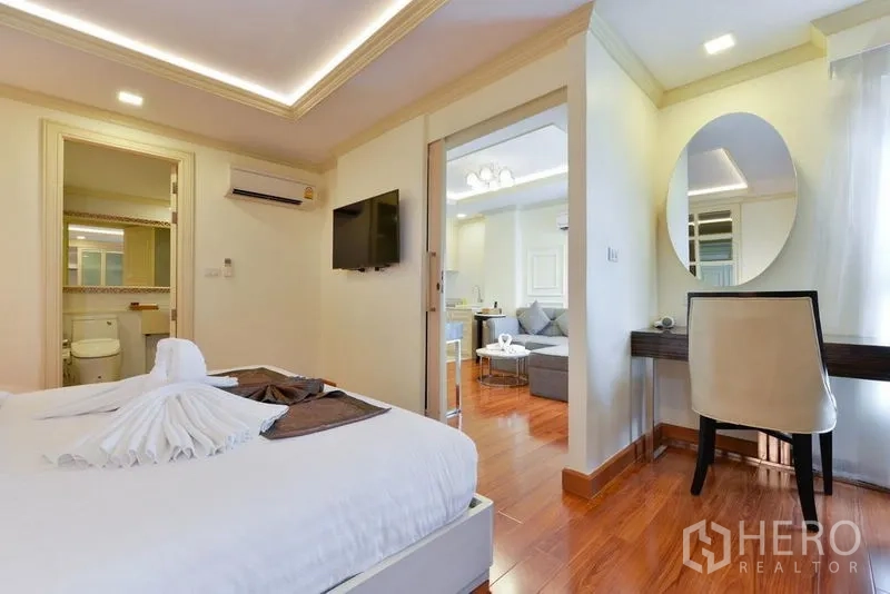 Apartment for rent in Khlong Toei, Bangkok - Bright 1-bedroom Thonglor apartment bedroom with TV, work desk, wood floors, and ensuite access.
