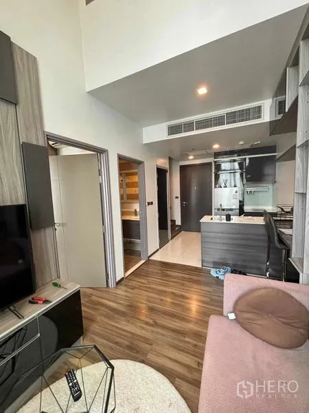Condominium for rent or sale in Watthana, Bangkok - Open-plan living and kitchen with wood flooring, TV cabinet and high ceilings.