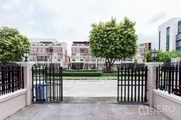 联排别墅 出租在Watthana, Bangkok - 从车道穿过黑色铁门望向绿树成荫的街道与对面联排