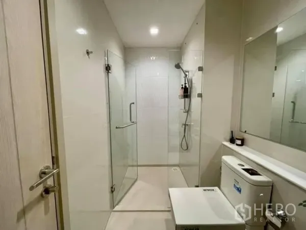 公寓 出租在Pathum Wan, Bangkok - 白色瓷砖浴室，玻璃步入式淋浴间与手持花洒。