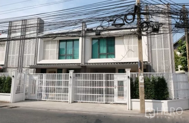 联排别墅 出租在Watthana, Bangkok - 两层联排别墅外立面，白色金属围栏与安静街景