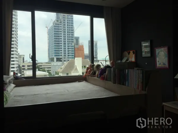 คอนโด ขายในWatthana, Bangkok - ห้องนอนพร้อมหน้าต่างบานใหญ่ เตียงแบบยกพื้น ชั้นหนังสือ และทิวทัศน์ตึกสูงของเมือง