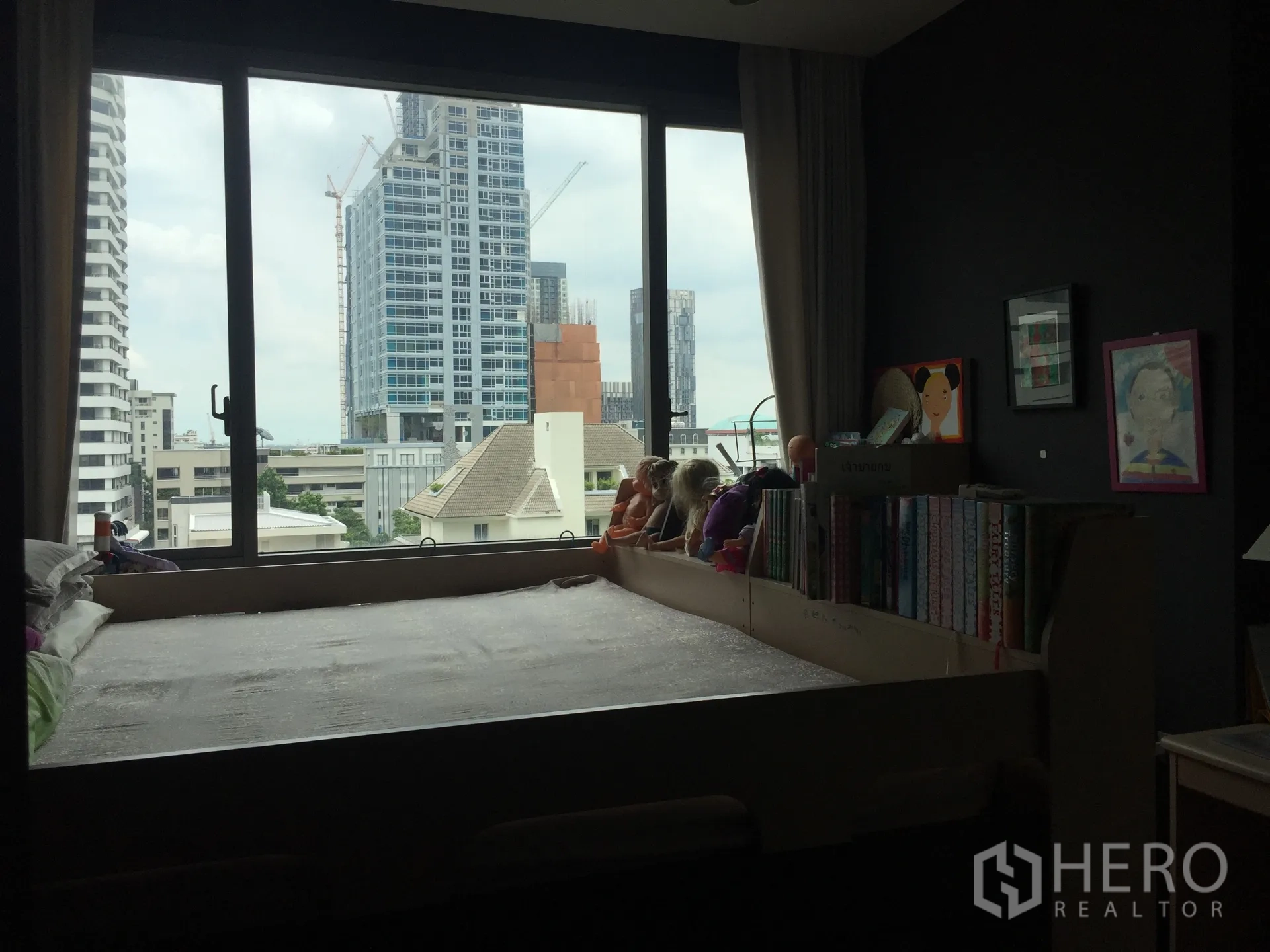 คอนโด ขายในWatthana, Bangkok - ห้องนอนพร้อมหน้าต่างบานใหญ่ เตียงแบบยกพื้น ชั้นหนังสือ และทิวทัศน์ตึกสูงของเมือง