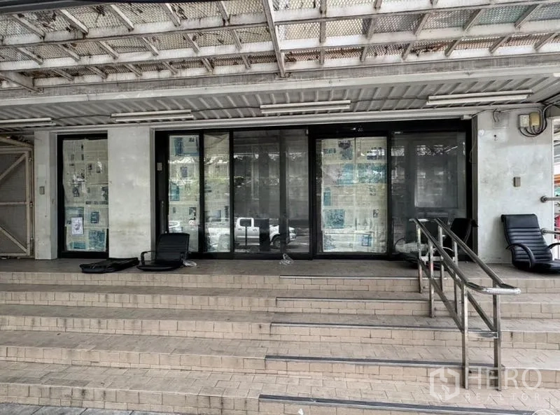 Shophouse for rent in Watthana, Bangkok - Streetfront shophouse entrance with wide steps, ramp and sliding glass doors under a metal awning.