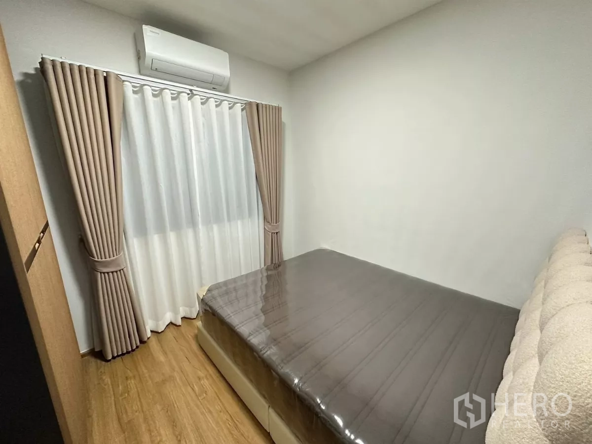 Townhouse for rent in Bang Phli, Samut Prakan - Guest bedroom view showing bed, wall AC and window drapes.