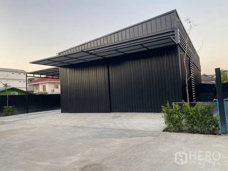 Warehouse for rent in Wang Thonglang, Bangkok - Entrance of black-clad warehouse with large doors, parking apron and perimeter fence.