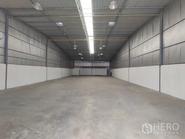 Warehouse for rent in Pathum Thani - Wide open storage hall showing high ceiling, insulated metal walls and central skylight lighting.