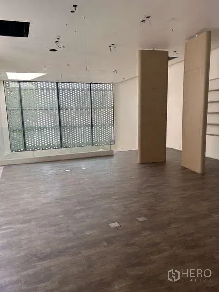 Standalone for rent in Khlong Toei, Bangkok - Open-plan showroom with wood flooring and a large patterned screen window bringing in light.