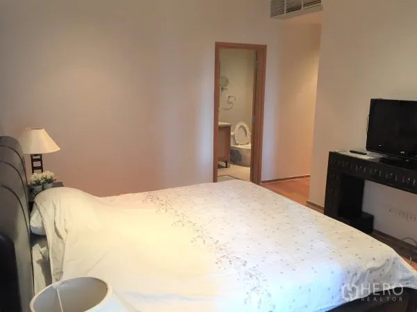 Condominium for rent in Khlong Toei, Bangkok - Cozy bedroom with TV console and direct access to an ensuite bathroom.