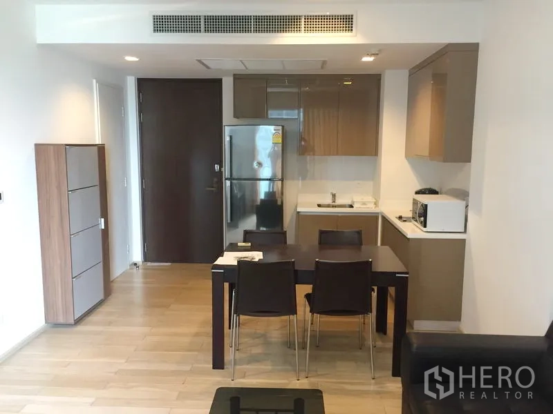 公寓 出租在Khlong Toei, Bangkok - 开放式厨房与餐区，亮面橱柜、不锈钢冰箱和四人餐桌的现代公寓。