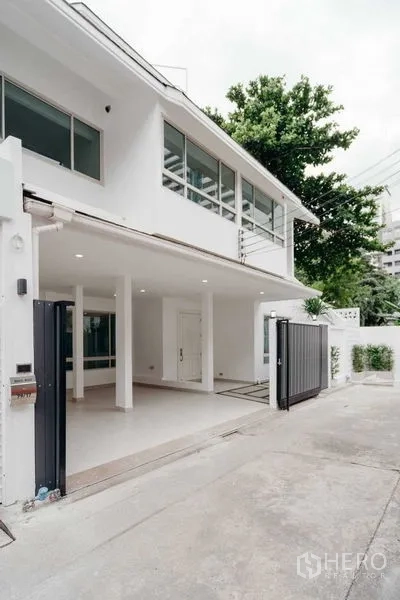 独立式住宅 出售在Watthana, Bangkok - 再次看到白色两层外立面，带车道与树木
